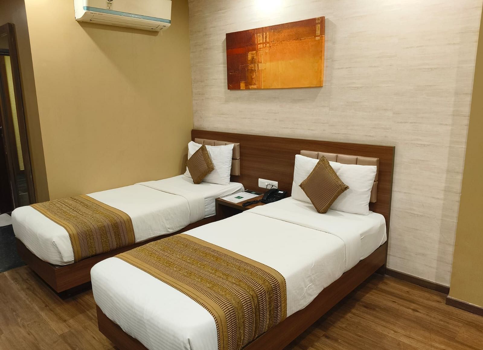 A side corner angle view of the room with twin beds, a wall frame, and an AC at Le ROI Digha Hotel, West Bengal.